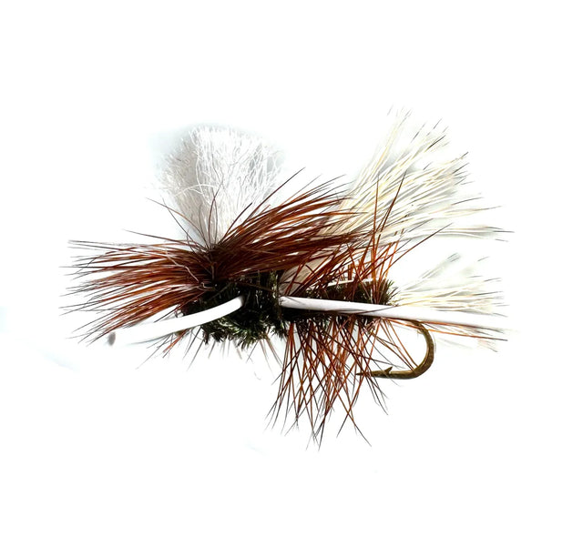 A close-up photograph showing the PMX Dry Fly Variant in sizes #12, #14, and #16. The flies feature a buoyant parachute post, natural body, and rubber legs, tied on barbed hooks as a versatile attractor for fast water.